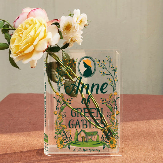 Acrylic Anne of Green Gables book vase with yellow and white roses on a pink tablecloth.