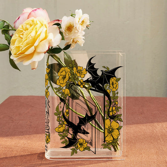 Acrylic book vase with dragon and yellow flower design holding fresh roses on pink table.